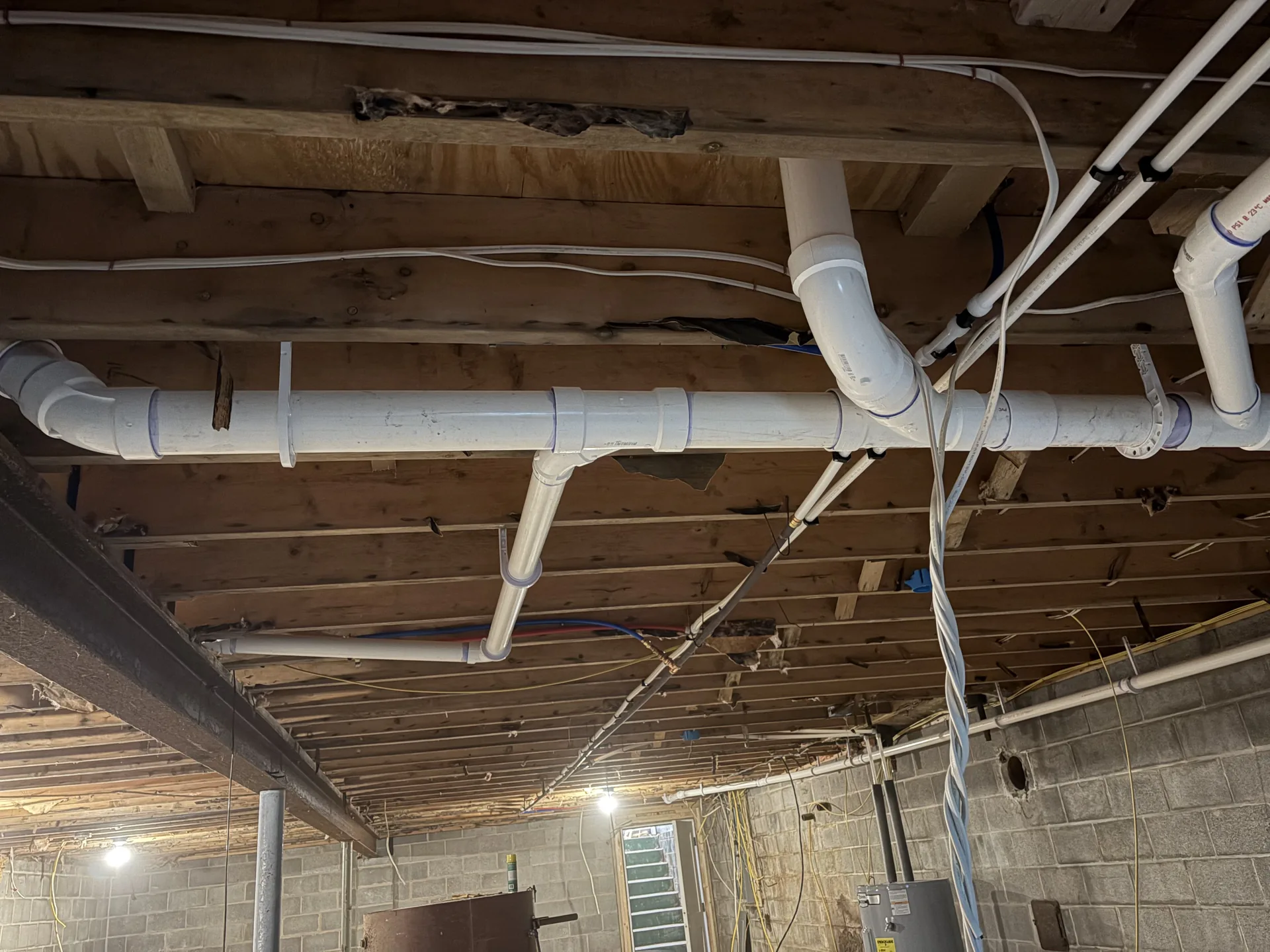 Overhead PVC drain rough-in installed between open basement floor joists.